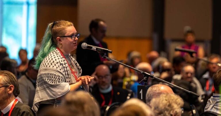 A young person speaking at a mic from a large crowd of delegates